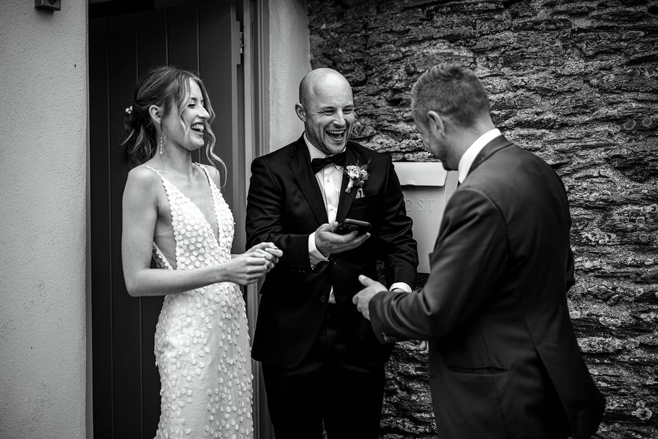 A bride and groom laughing together as Lewis Belcher performs close-up magic for them.