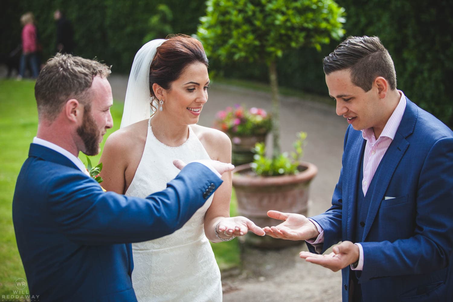 Lewis Belcher performing close-up magic for a couple during an outdoor wedding reception.